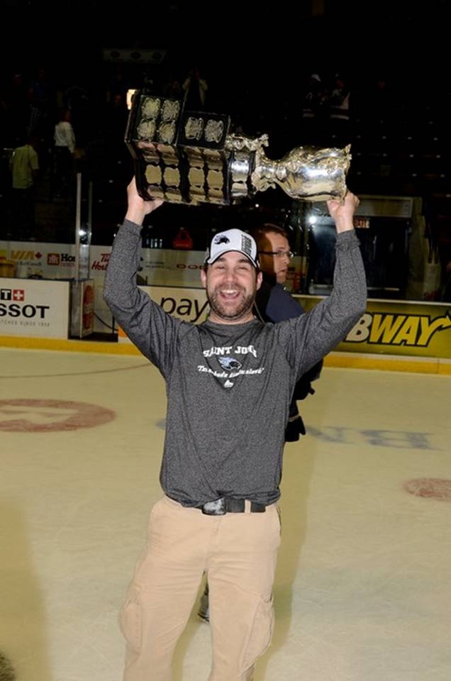 Jeff Kelly in a hockey rink holding a trophy above his head